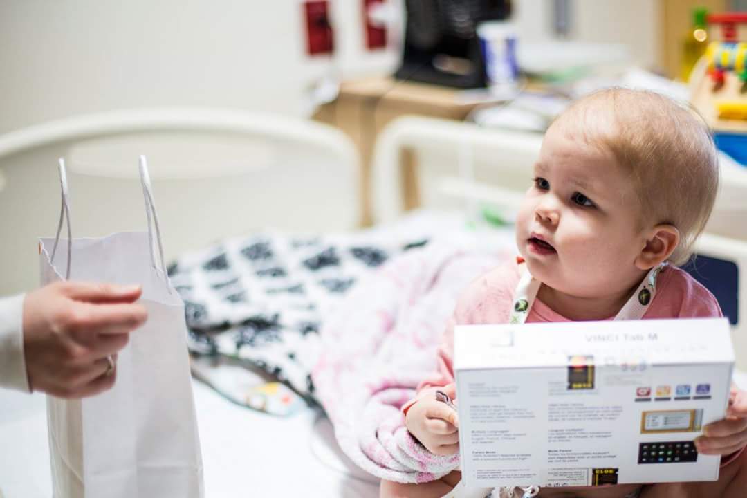 A young hospital patient receiving a handheld gaming device at the bedside
